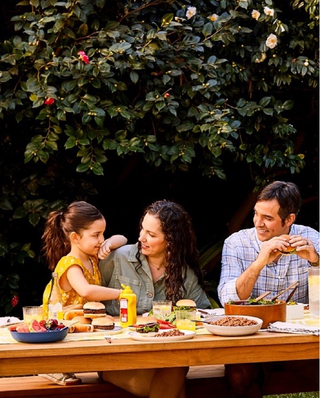 A family having a picnic at a picnic table near the woods.