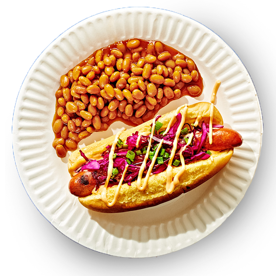 Top Down view of shishito slaw hot dog on a paper plate next to baked beans