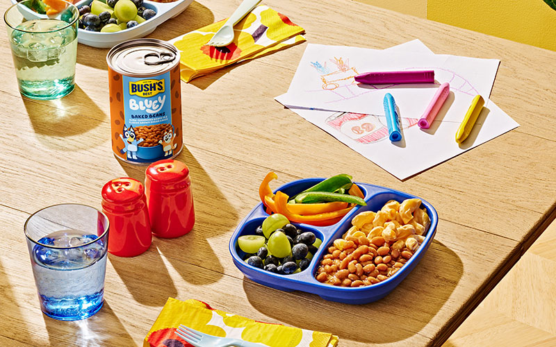 Blue plate with Bluey Baked Beans, mac and cheese, bell peppers, and grapes.