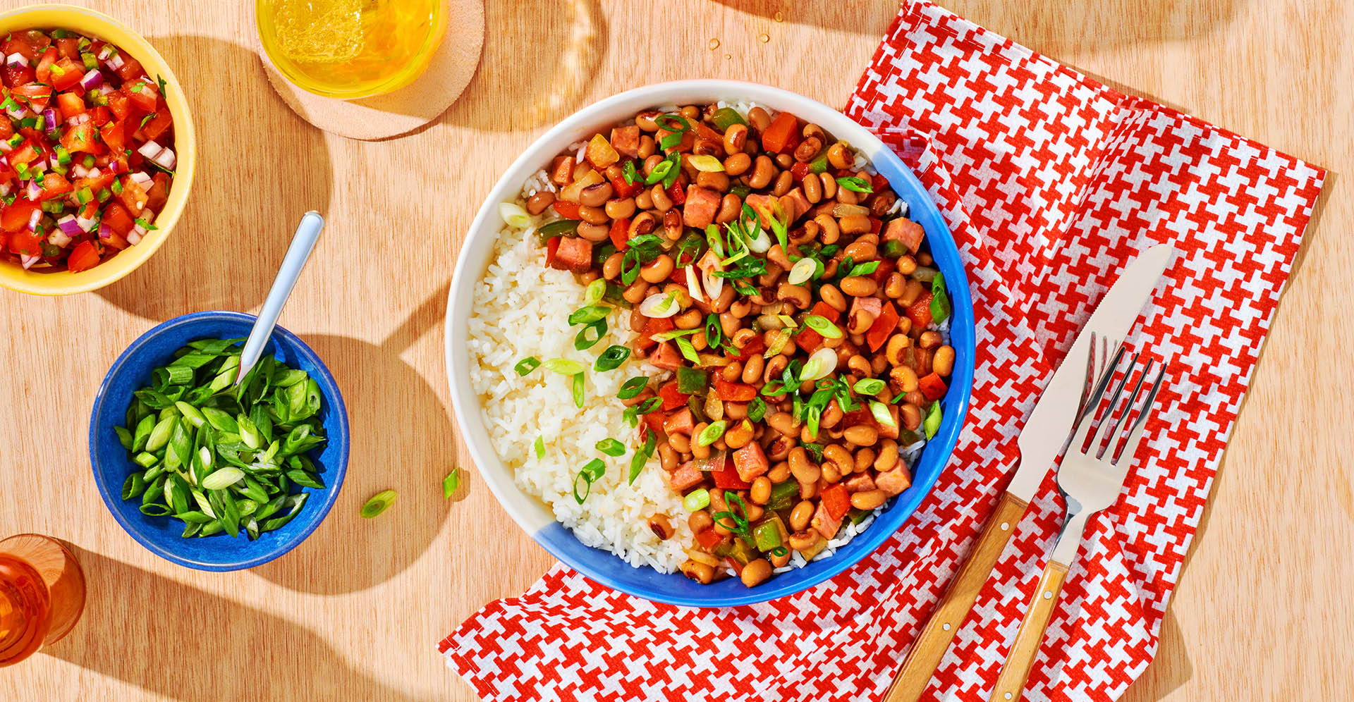 Bowl of Hopping John and rice in bowl with sides of tomato and green onion. 